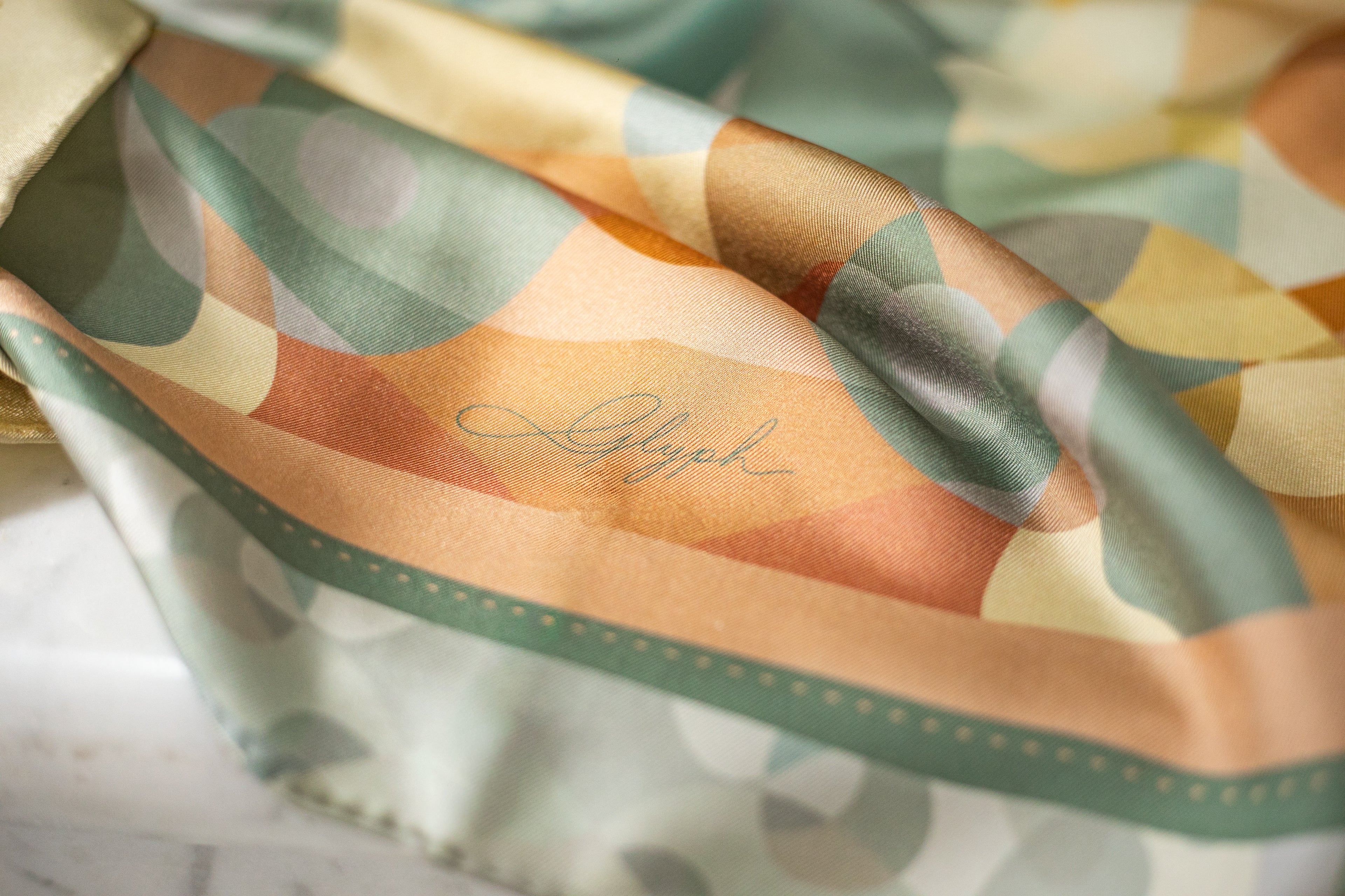 Close-up of the Harmony silk scarf by Glyph, showing the silk twill texture, artwork details and Glyph signature.