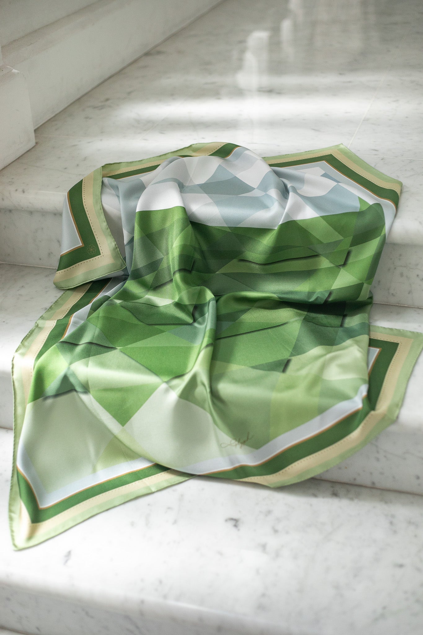Quiet Horizon silk scarf by Glyph draped on marble steps, highlighting its layered green geometric design and fluid silk texture.