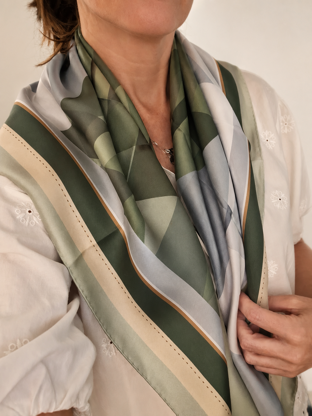 Quiet Horizon silk scarf by Glyph worn around the neck, featuring layered geometric forms in olive green, soft blue and cream.