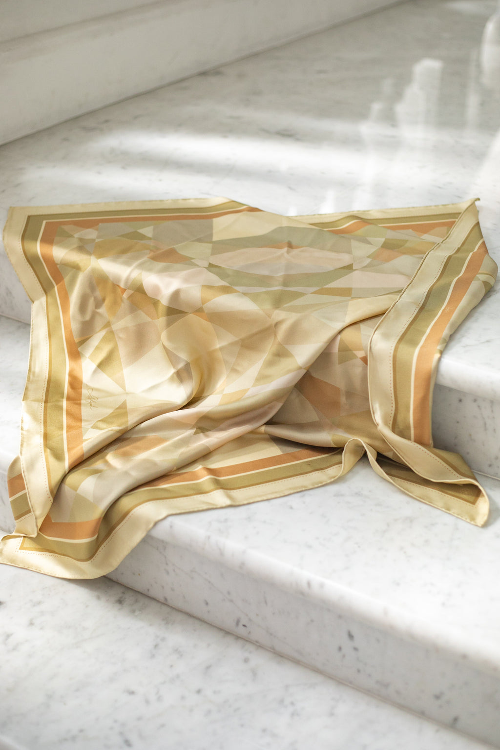 Soft Structure silk scarf by Glyph draped on marble steps, highlighting its warm neutral geometric design and fluid silk texture.