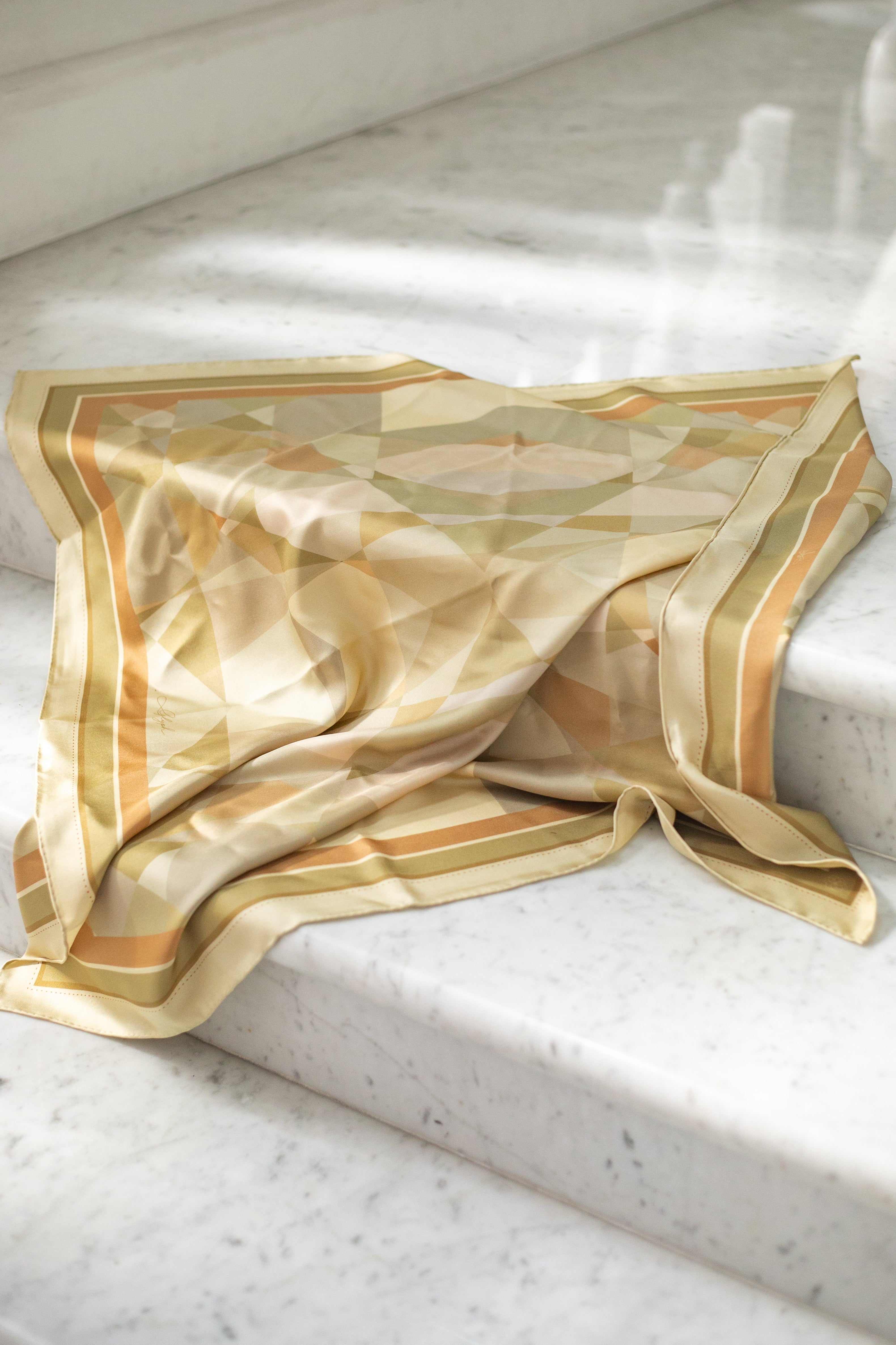 Soft Structure silk scarf by Glyph draped on marble steps, highlighting its warm neutral geometric design and fluid silk texture.