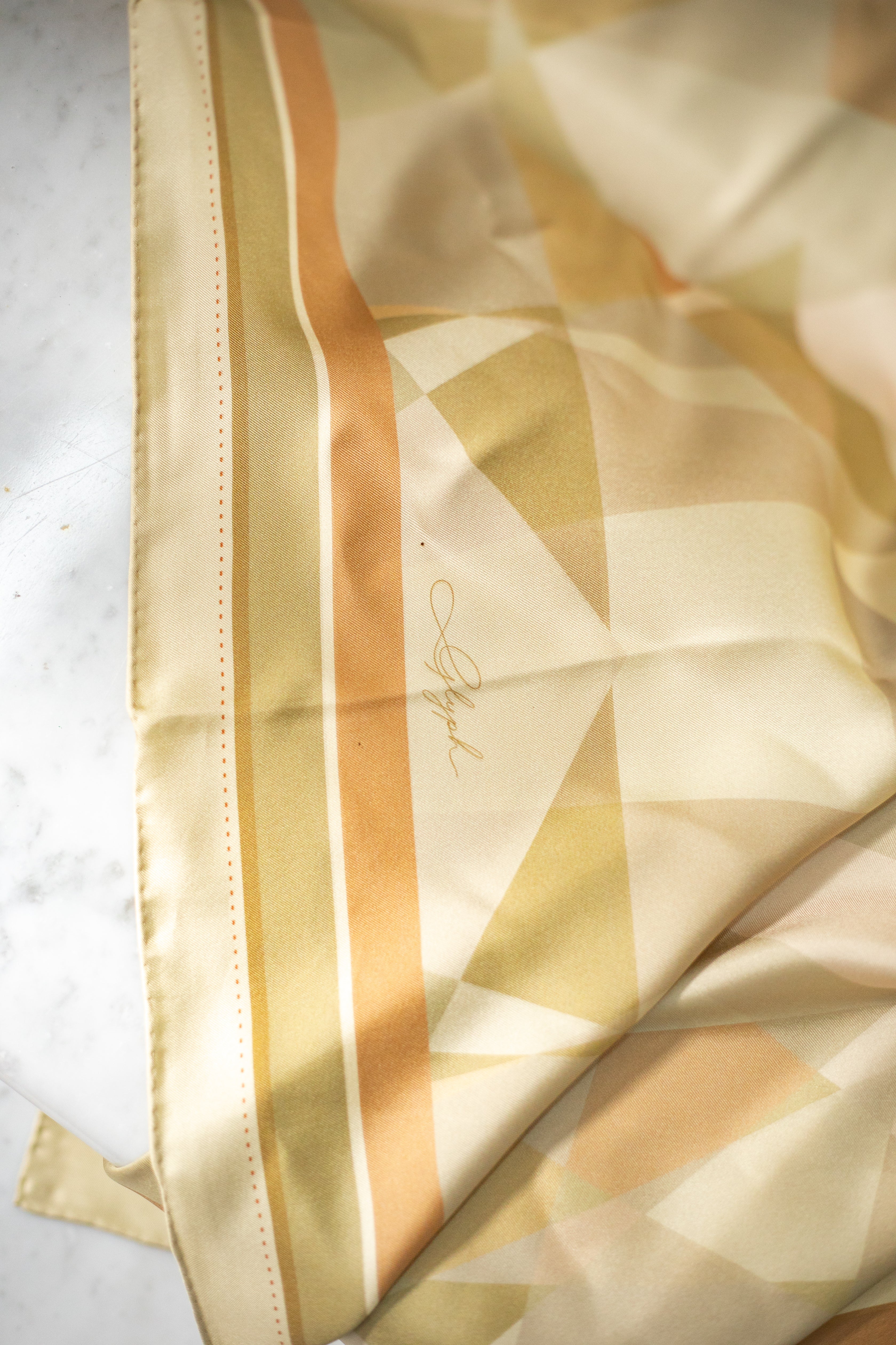 Close-up of the Soft Structure silk scarf by Glyph, showing the signature detail, warm neutral geometric pattern and hand-rolled edge.